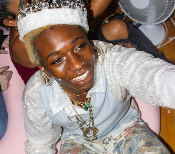Person in sparkly clothes and crown smiling up at camera