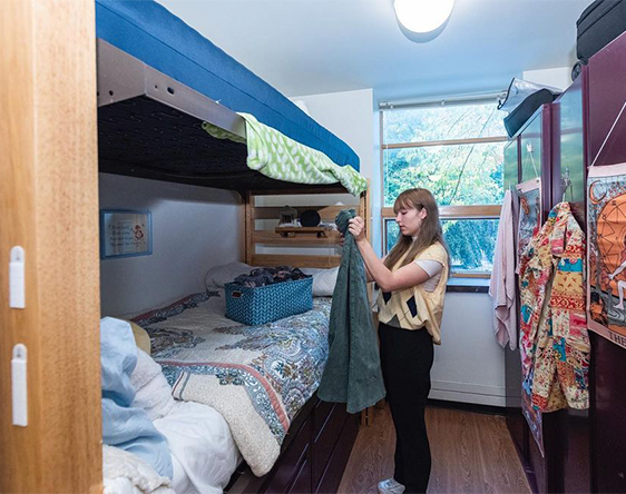 student folding clothes in bedroom of dorm